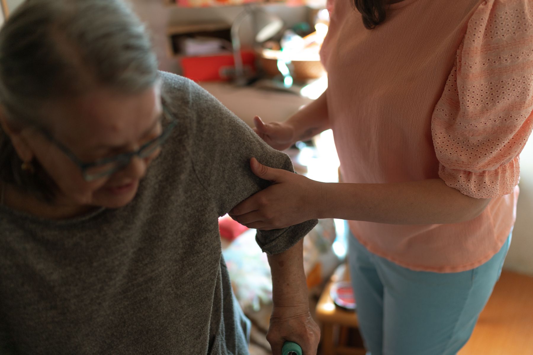 A caregiver gently assists an older woman at home.