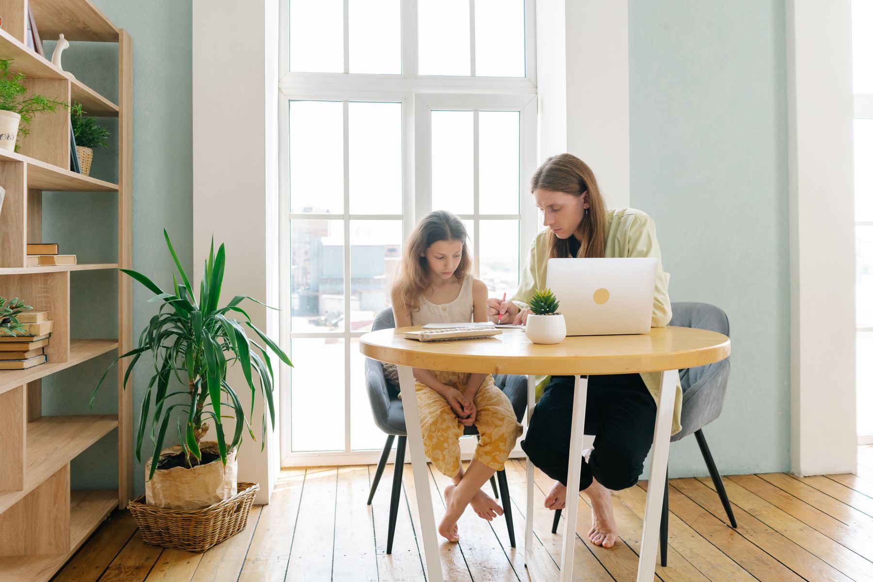 A parent and child work together with a notebook and laptop at home.